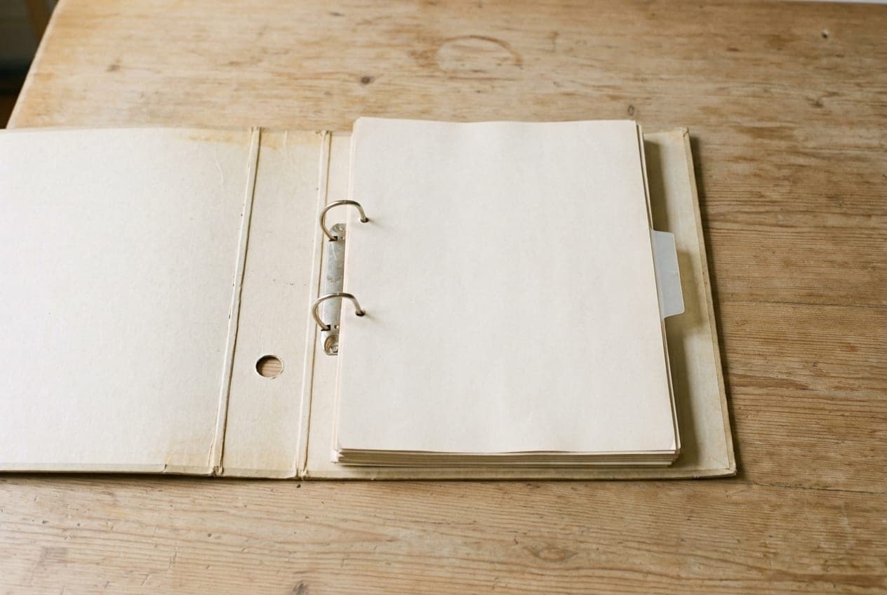 Una carpeta de anillas abierta, con hojas en blanco, sobre una mesa de madera